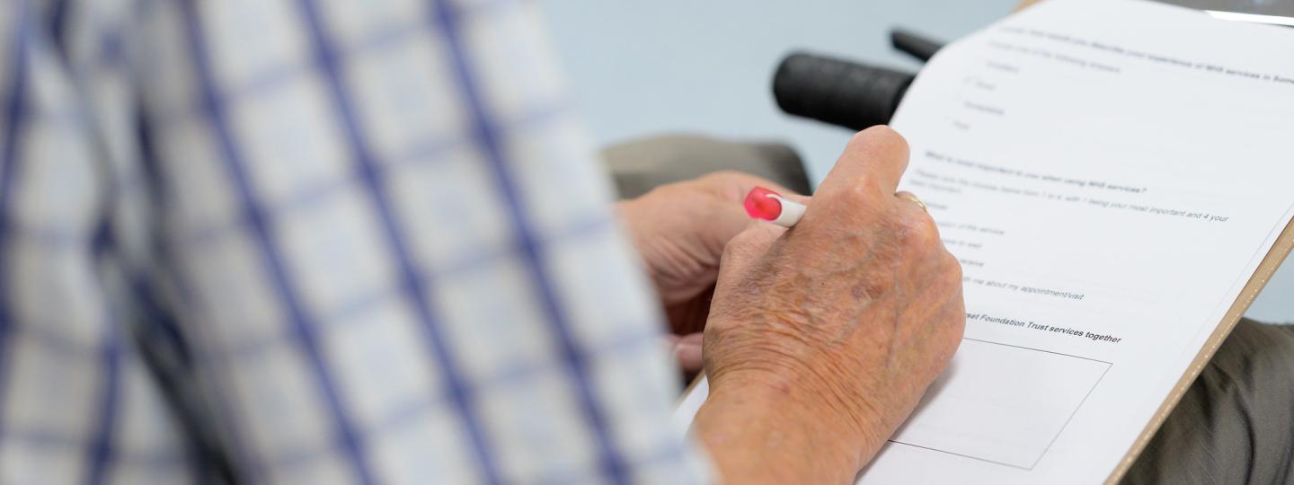 A photograph of a man filling in a feedback form on a clipboard